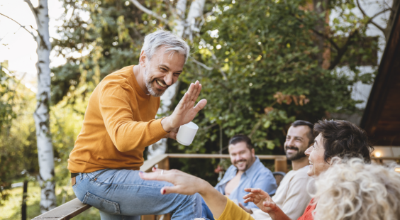 Image d’un homme souriant assis sur une rambarde et faisant un signe de main aux personnes en face de lui